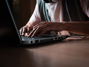 A young man with long hair is working on a laptop. hands close up